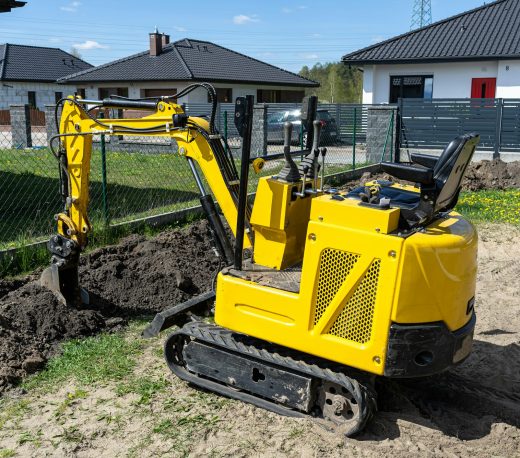 Mini digger digging a hole in the garden along the fence to the drainage pipes.